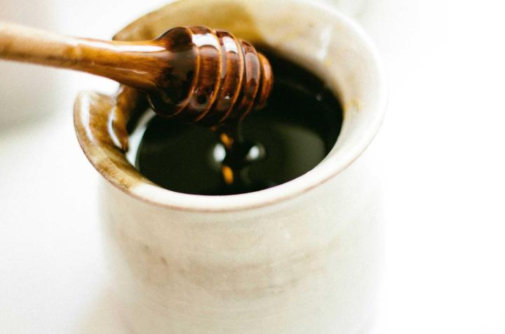 Honey dripping from a wooden dipper into a white pot