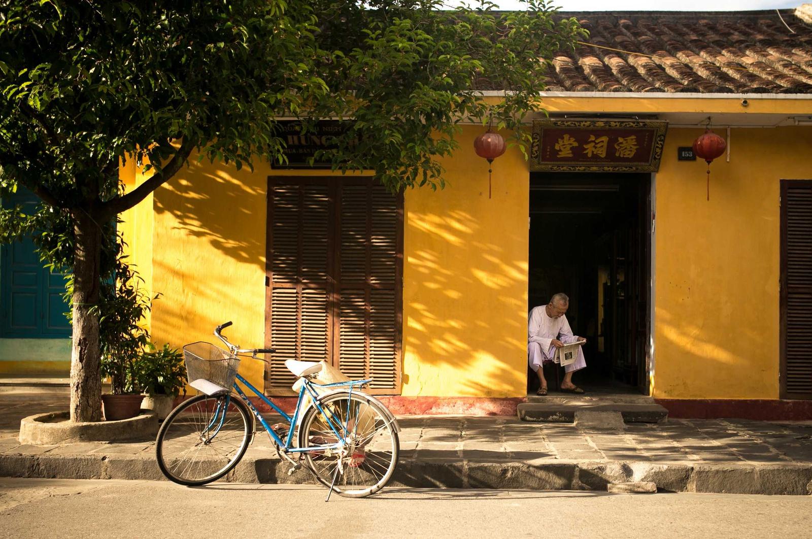 A bicycle parked outside a yellow shopfront under a tree