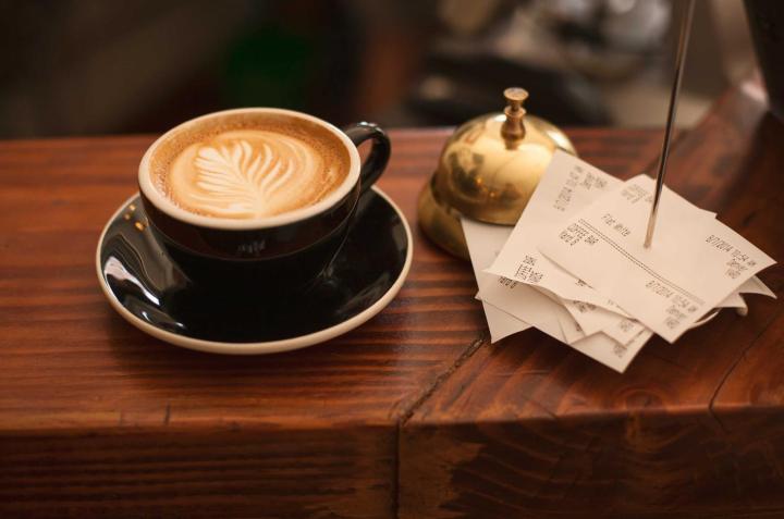 A latte beside a bell and order slips on a café counter