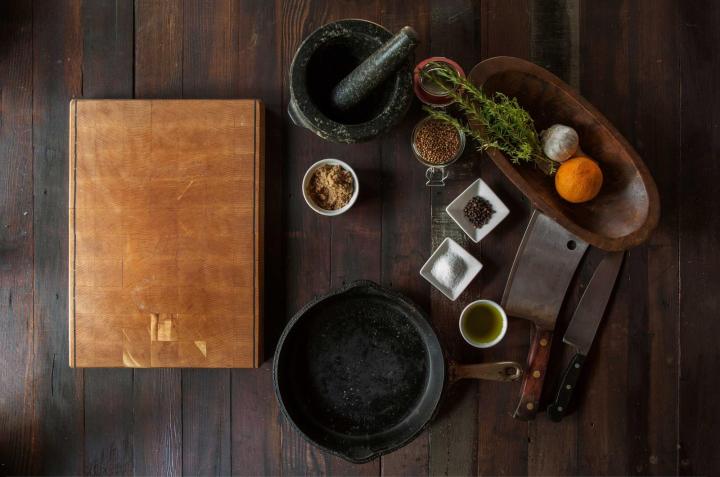 A chopping board, cast-iron pan, mortar and spices on a dark wooden table
