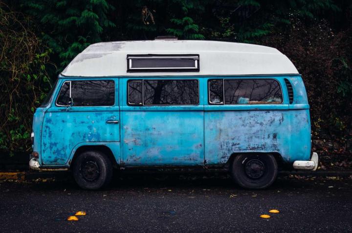 A weathered blue camper van parked under trees